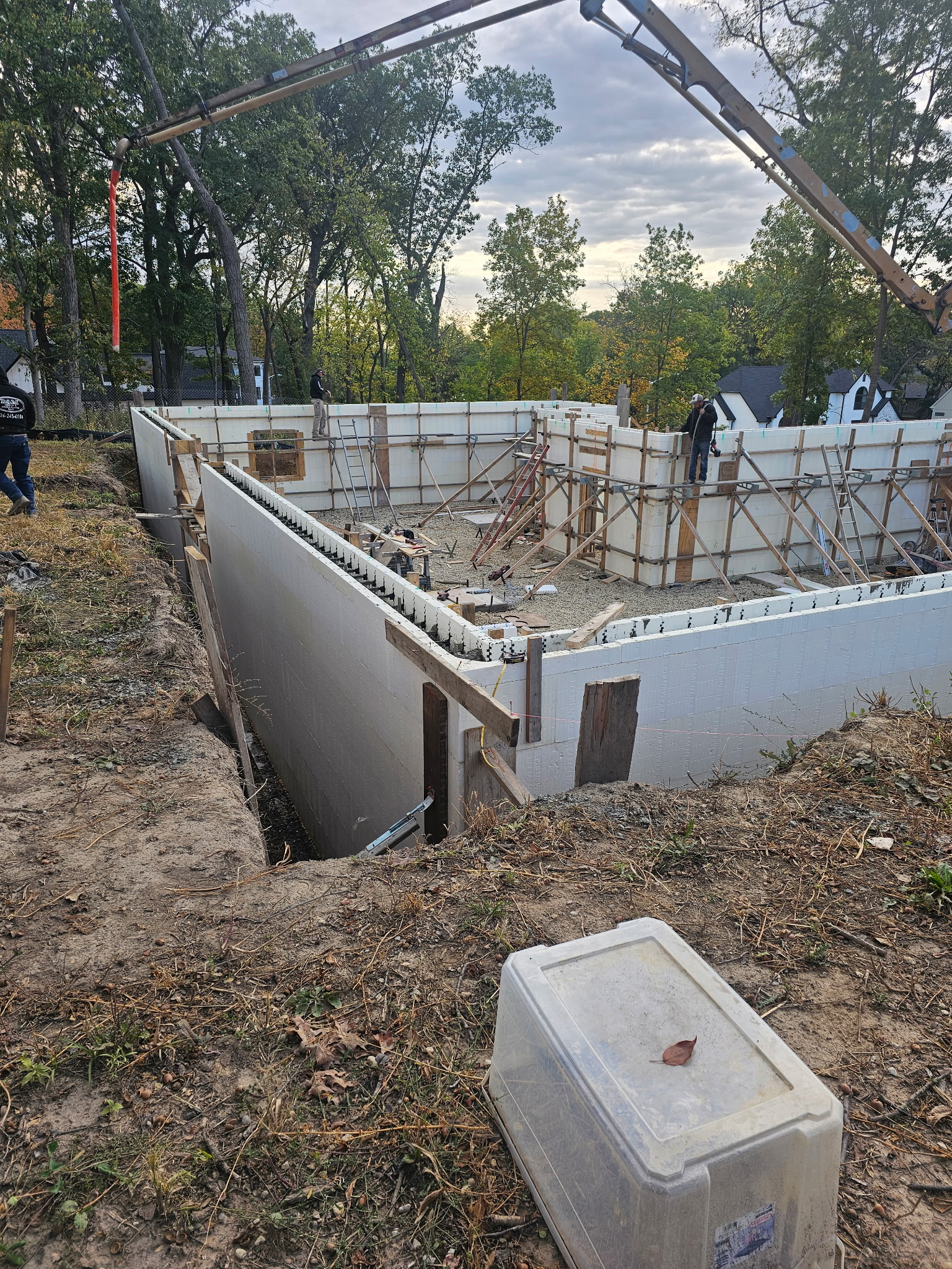 A concrete worker holds a tape measure across a prepared project area while marking the layout with the other hand